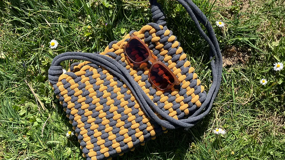 Knitted bag and sunglasses on grassy field.