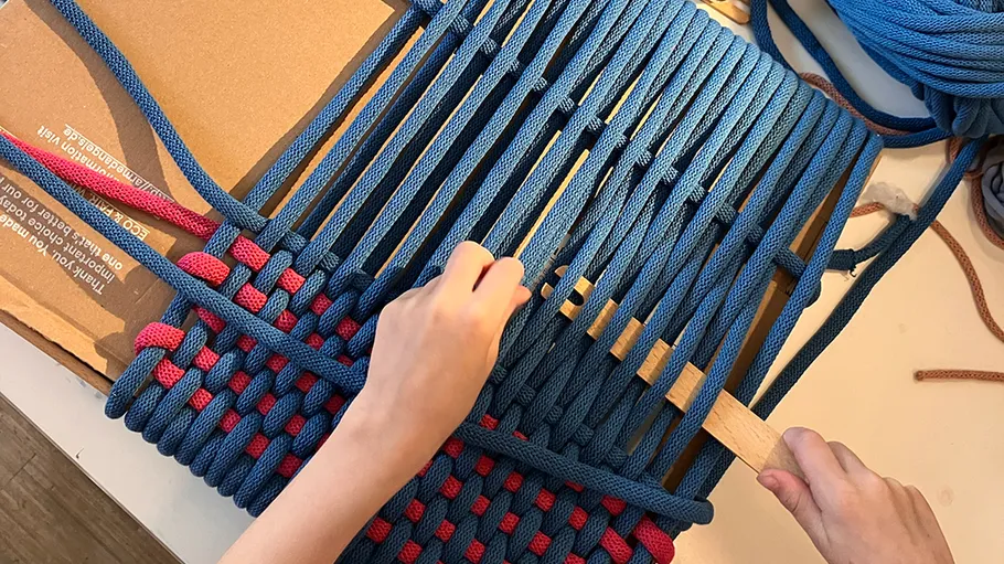Hände flechten blaue und rote Seile auf Pappe.