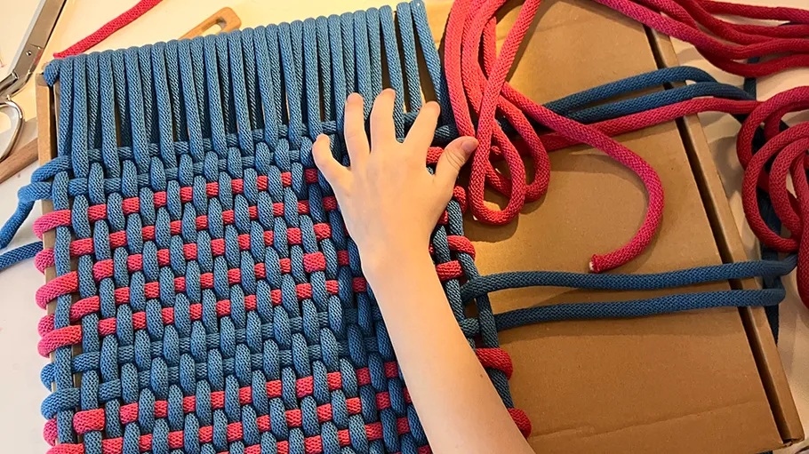 Hand webt ein blau-rotes Seilmuster.