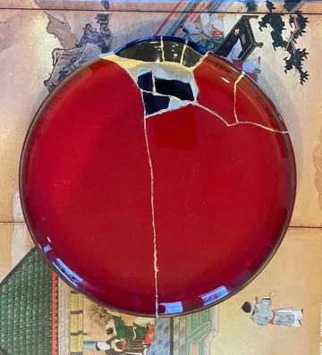 Red plate repaired with gold on illustrated background.