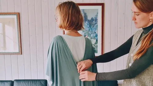 Two women adjusting a dress in a living room.
