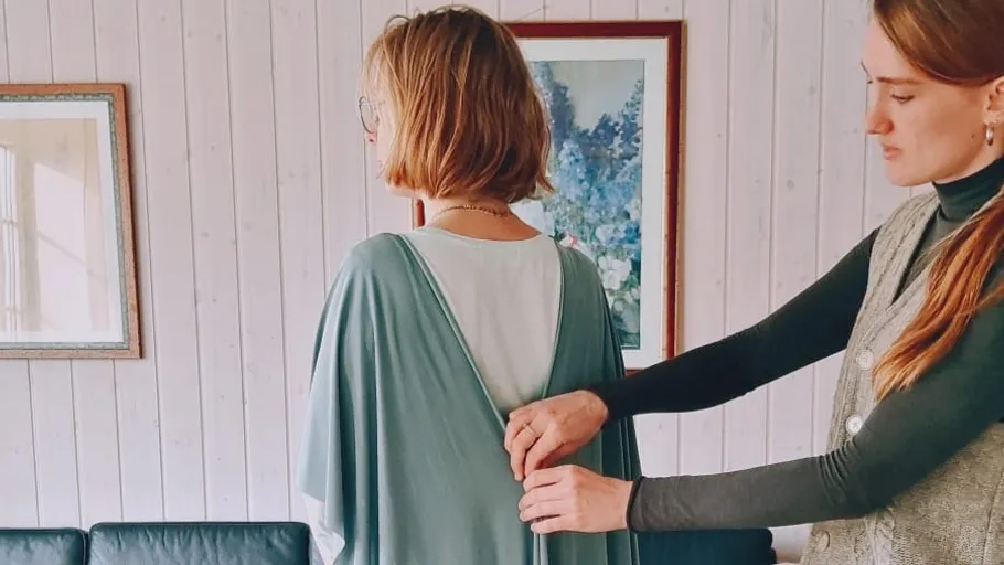 Zwei Frauen justieren ein Kleid im Wohnzimmer.