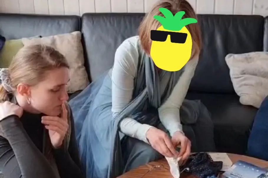 Two people sitting at a table, one sewing.