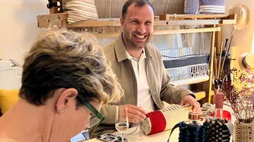 Mann lächelt am Basteltisch mit Webausrüstung.