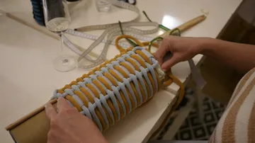Hands weaving colorful ropes around an object.