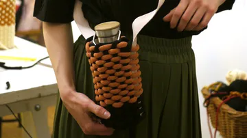 Person hält Metallflasche in gewebtem Halter.