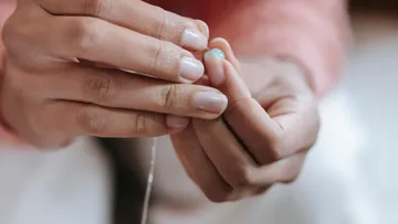 Hands stringing a turquoise bead on thread.