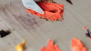 Palette knife mixing orange paint on palette.