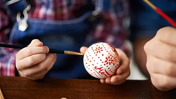 Child painting Easter egg at table.