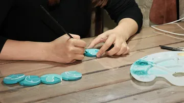 Person painting teal stones on wooden table.