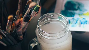 Paintbrushes in jar beside watercolor painting.