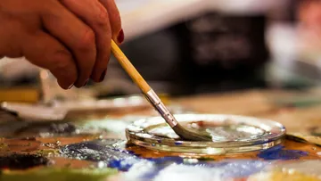 Hand holding paintbrush on palette.