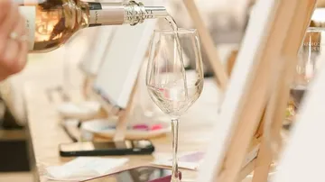 Wein wird ins Glas nahe Staffeleien gegossen.