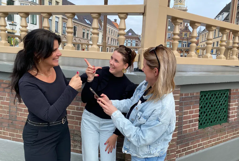 Three women smiling and using a smartphone outdoors.