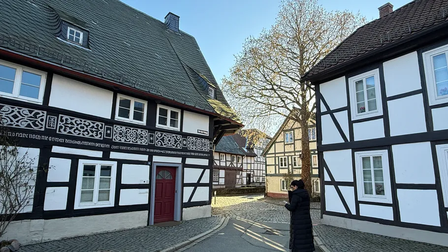 Person in black coat walks between timber houses.