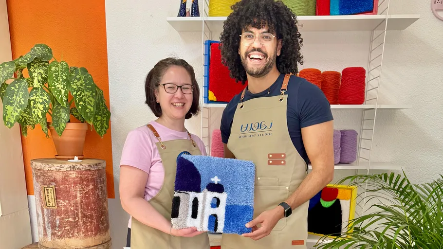 Two people holding colorful textile art indoors.
