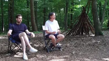 Two men sitting in forest near teepee.