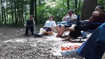 Personen sitzen im Wald, entspannen auf Stühlen.