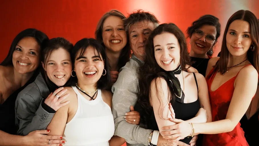 Group of people smiling in front of red background.