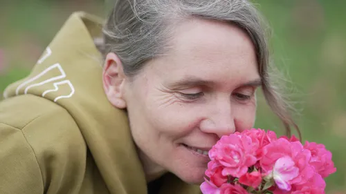 Frau riecht rosa Blumen draußen.
