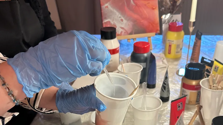 Person mixing paint in a cup, art supplies nearby.
