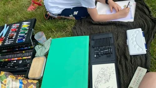 Person zeichnend auf Papier, umgeben von Kunstbedarf.
