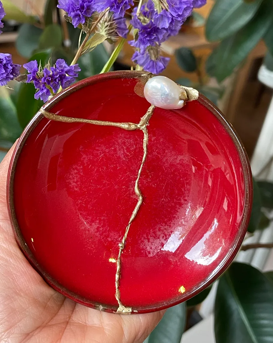 Red plate with gold repair, purple flowers background.