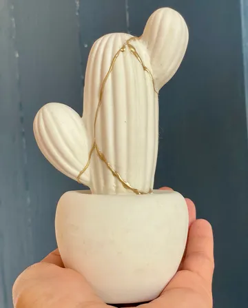 Weißer Keramik-Kaktus mit Goldreparatur, handgehalten.