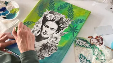Person malt Frida-Kahlo-Leinwand mit Blumendesign.