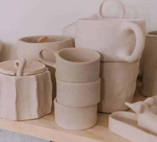 Clay pottery mugs on wooden shelf displayed.