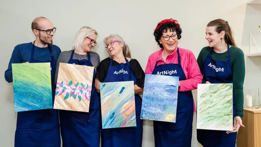 Five people holding individual paintings, smiling indoors.