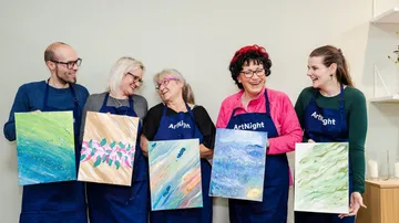 Five smiling people holding paintings in art class.