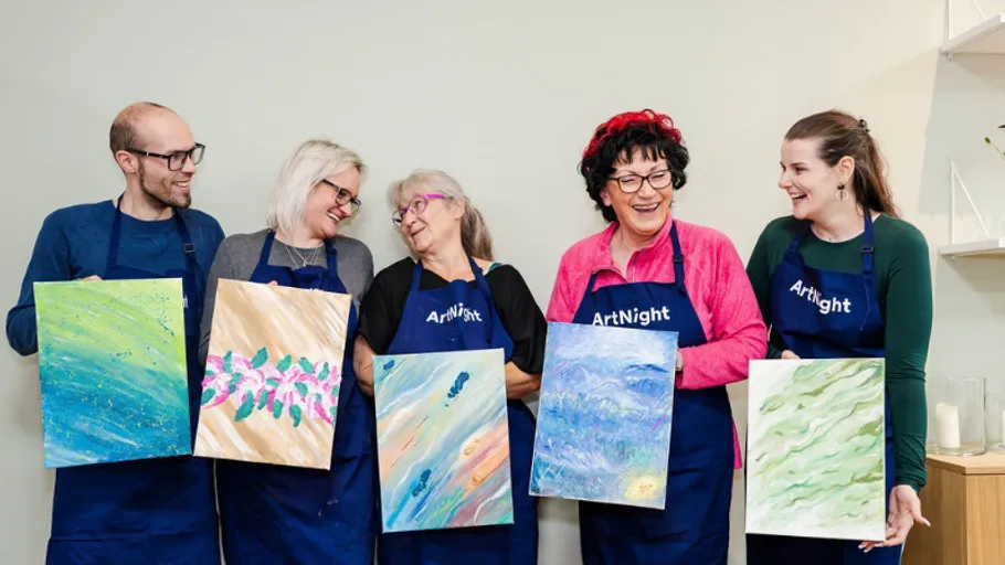 Five people showing paintings, wearing aprons, indoors.