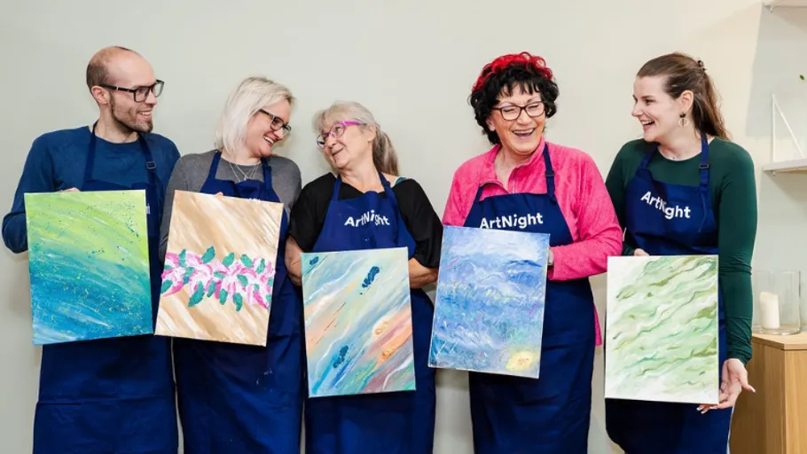 Five people holding paintings, smiling indoors.