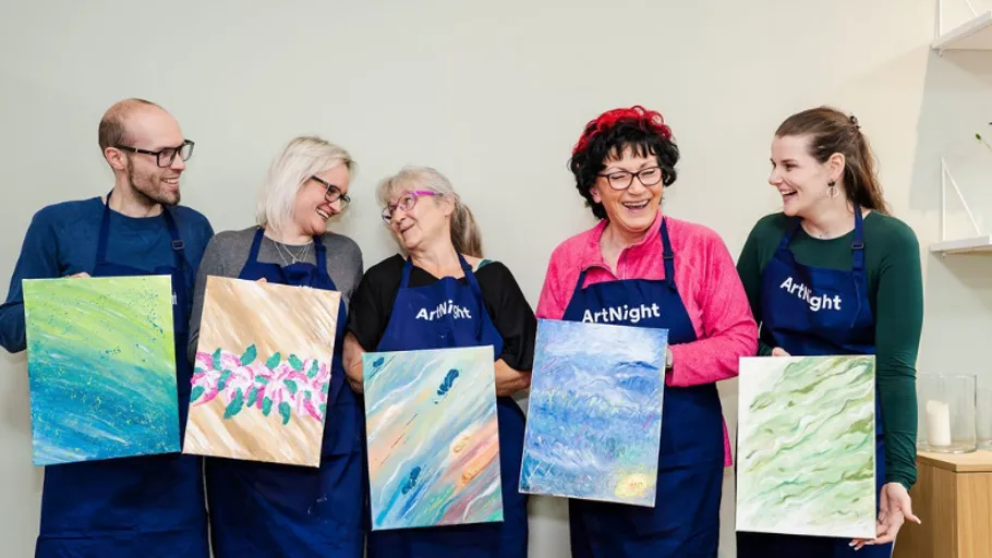 Five people smiling, holding colorful paintings indoors.