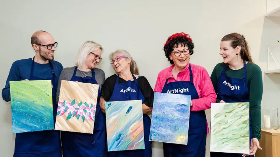 Group holding paintings, smiling, in art class.