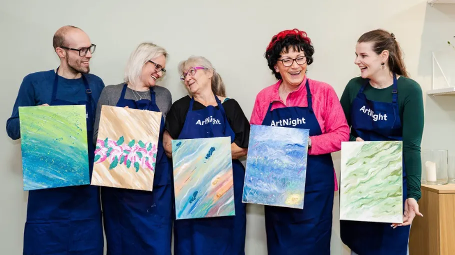 Five people holding paintings, smiling in studio.