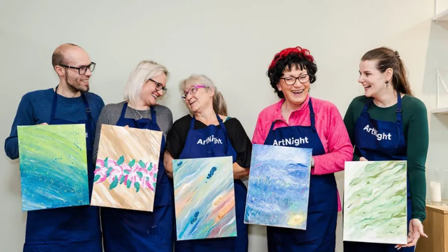 Five people holding colorful paintings, smiling indoors.