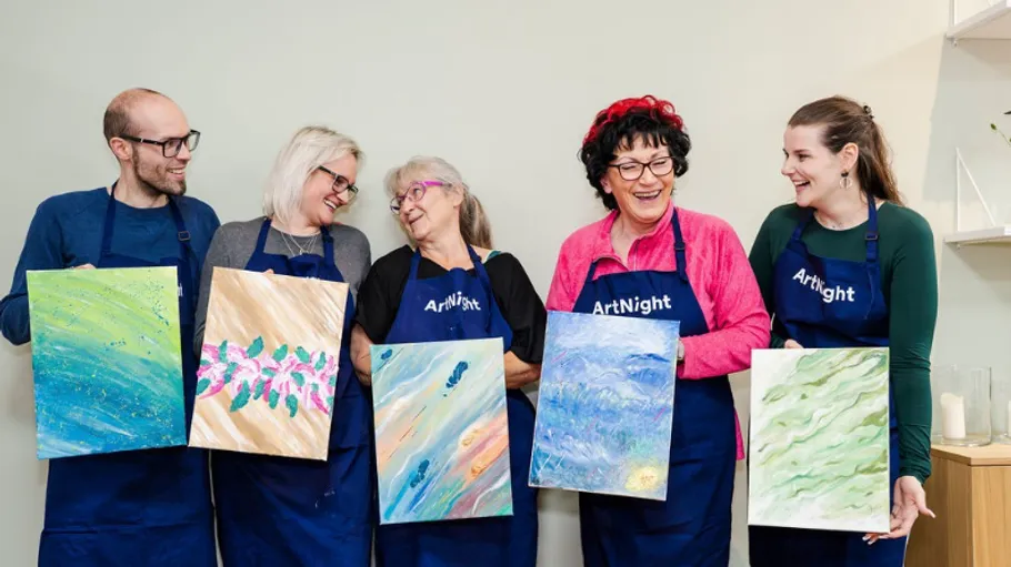 Five people smiling, holding paintings in art class.
