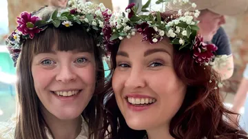 Zwei Frauen lächeln mit Blumenkronen drinnen.