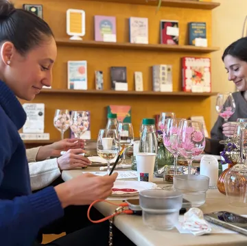 Frauen bemalen Weingläser an einem Tisch.