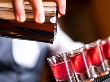 A bartender pours cocktails into glasses at the bar.