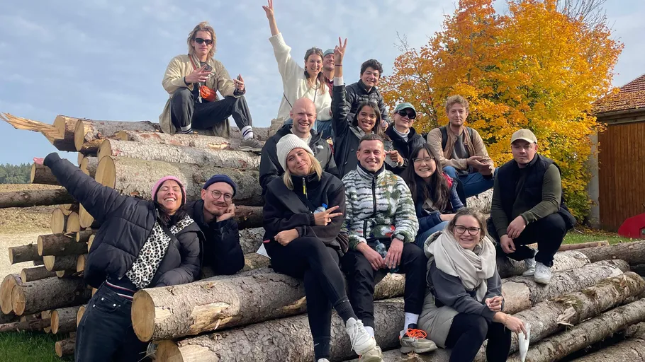 Group posing on stacked logs, autumn backdrop.