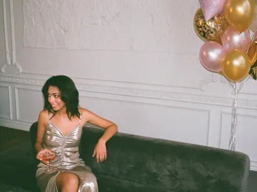 Woman in shiny dress sits and smiles on sofa.