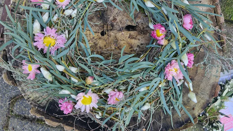 Floral wreath on wooden tree stump outdoors.