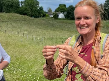 Frau hält etwas mit schmalen Fingern in einer Wiese.