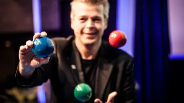 Mann jongliert bunte Bälle drinnen.