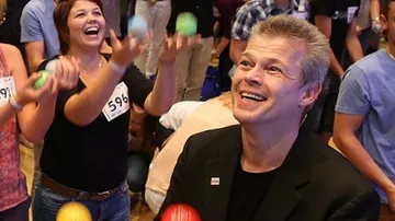 People joyfully juggling colorful balls indoors.