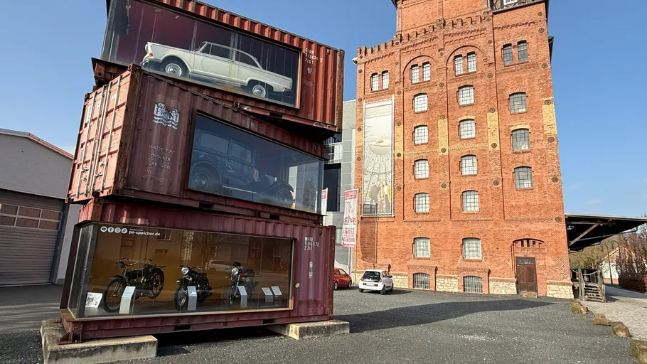 Stacked shipping containers display vintage vehicles outside.