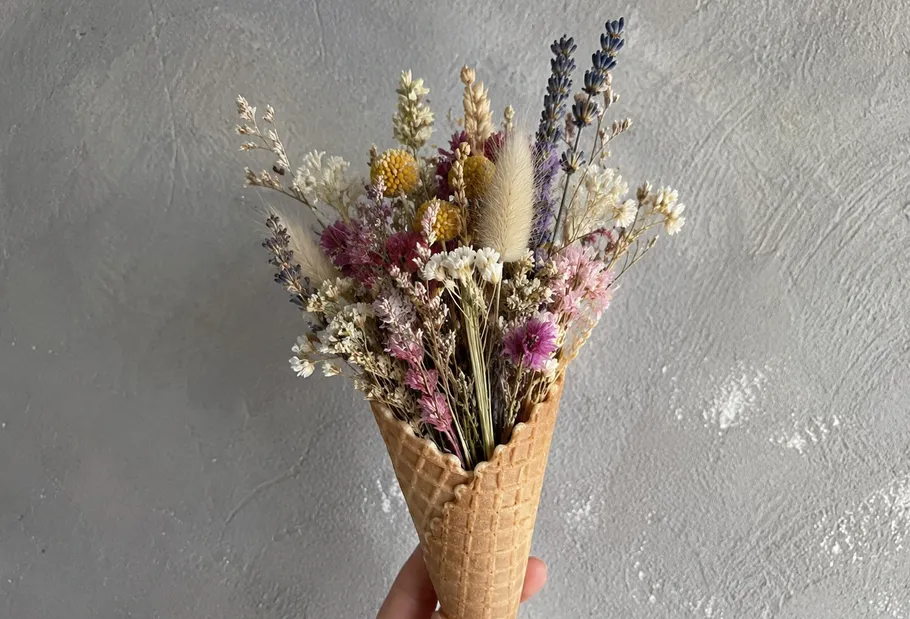 Hand holding ice cream cone with dried flowers.